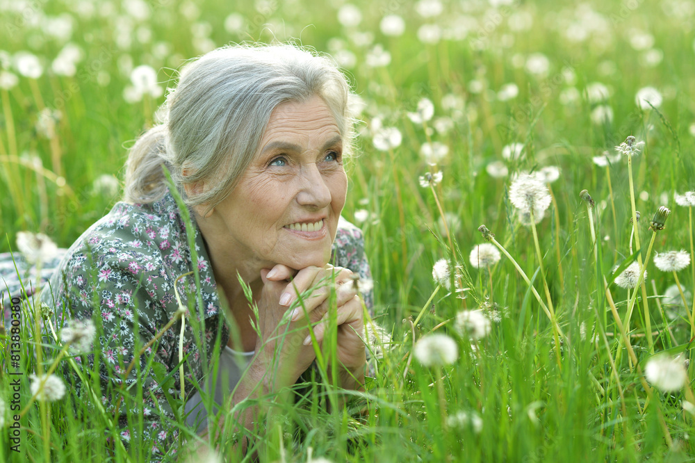 Portrait of a beautiful senior woman in green field with dandelions