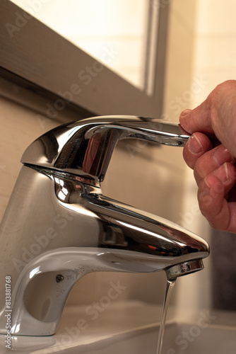 Close-up of a tap in a bathroom and a hand closing the tap. .General drought concept. photo