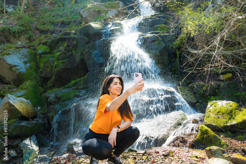 Woman standing in front of waterfall making selfie pictures