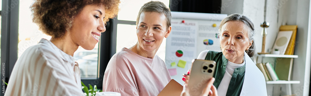 Cheerful diverse businesswomen engaged with cell phone.