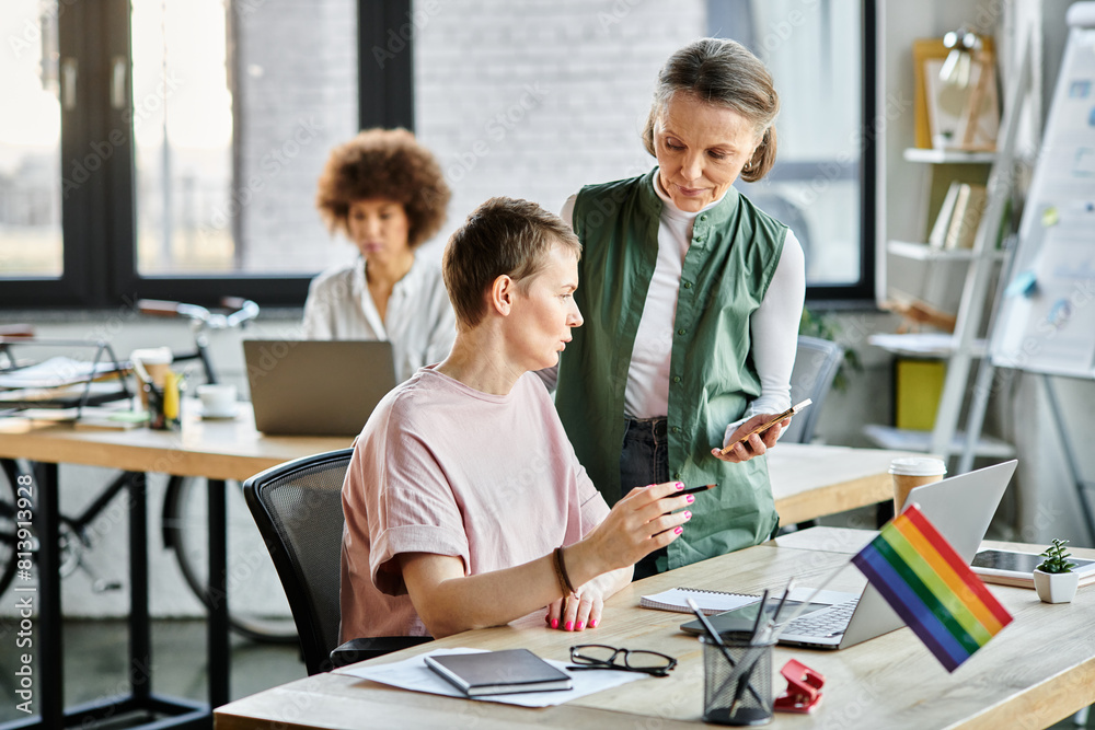Appealing diverse businesswomen working together on project in office, pride flag. Appealing diverse businesswomen working together on project in office, pride flag.