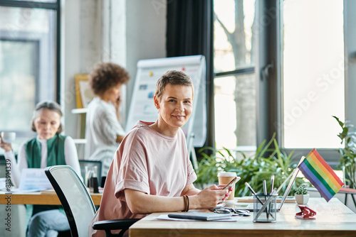 Cheerful woman engrossed in work, with phone, with her diverse colleagues on backdrop.