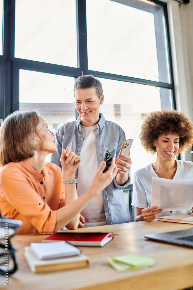 Diverse group of businesswomen focused on a cell phone at a table. Diverse group of businesswomen focused on a cell phone at a table.