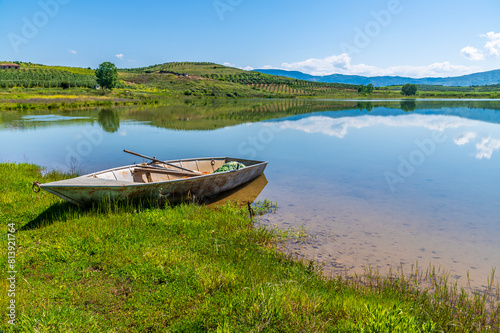 A view past a boat out across a lake at Belsh lakes in Albasan county, Albania in summertime © Nicola