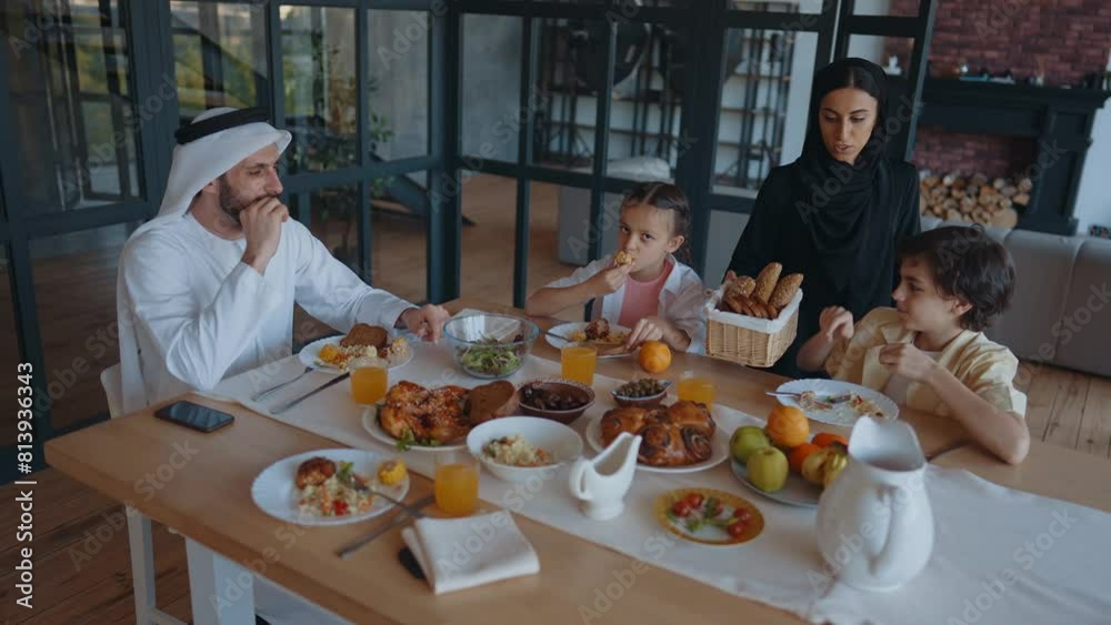Arabian family from Dubai having lunch together in a cozy apartment. Kids with traditional parents wearing emirati kandura and abaya. Arabian family from Dubai having lunch together in a cozy apartment. Kids with traditional parents wearing emirati kandura and abaya.