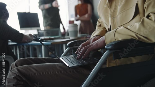 Close up view of young man with disability sitting in wheelchair and typing on laptop while working in office
