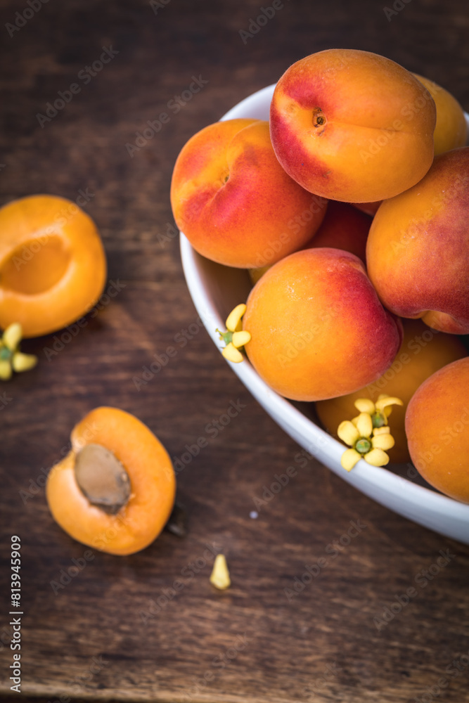 White ceramic bowl with ripe apricots on a wooden table in the garden