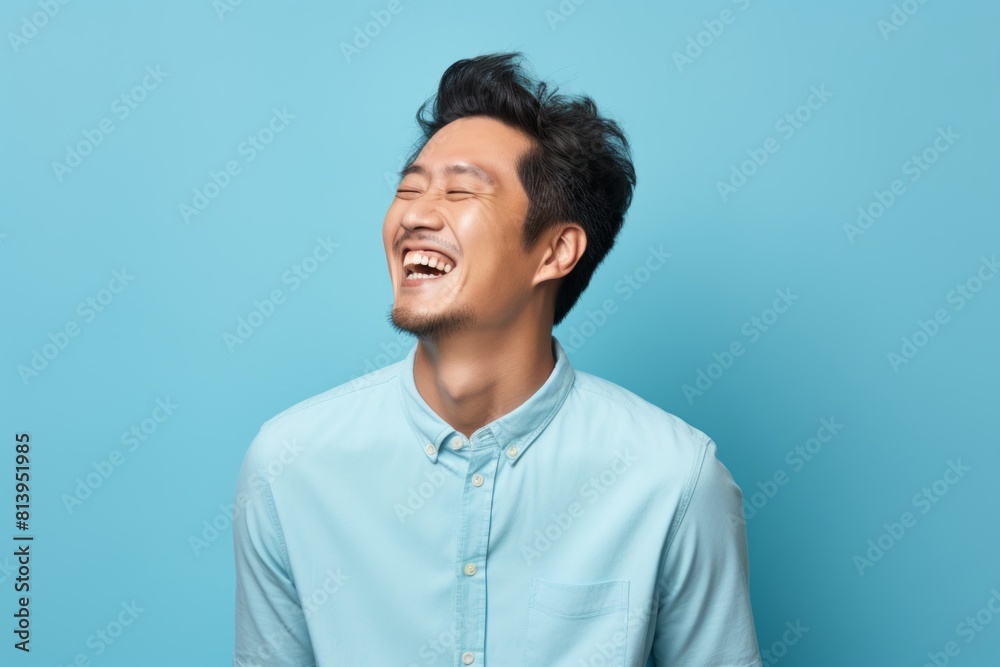 Portrait of a blissful asian man in his 30s laughing in pastel blue background Portrait of a blissful asian man in his 30s laughing in pastel blue background