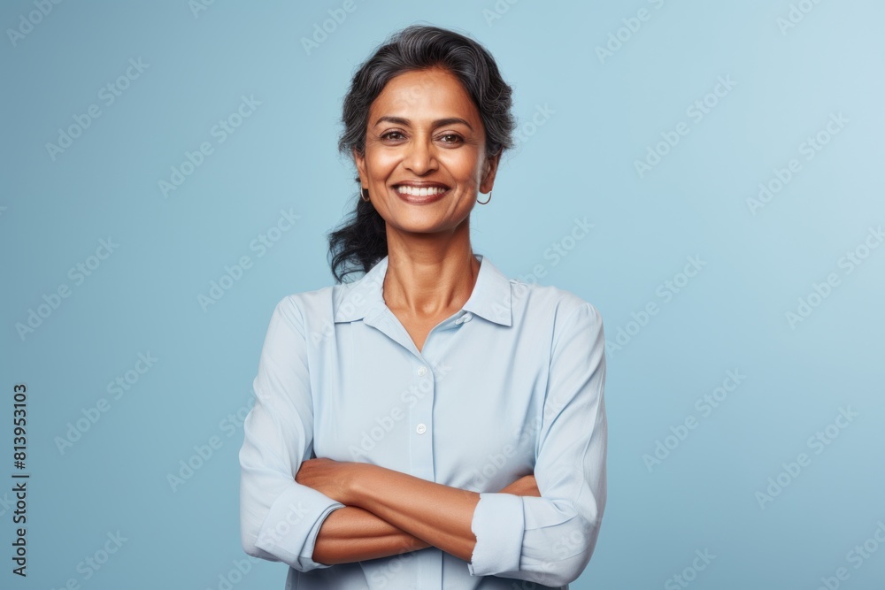 Portrait of a merry indian woman in her 50s with arms crossed on pastel blue background Portrait of a merry indian woman in her 50s with arms crossed on pastel blue background