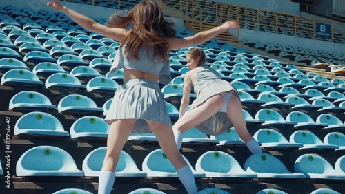 Two fiery women joyfully dancing on a stadium track. Slow motion shooting. Women cheerleaders in short skirts happily dancing on the running track. Two girls in bras seductively dancing together on a 