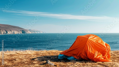 An orange tent on a grassy field with a view of the sea and clear sky on a sunny day.
