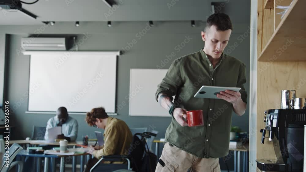 Young man with prothetic leg using digital tablet, taking mug with coffee from espresso machine and going to work in office Young man with prothetic leg using digital tablet, taking mug with coffee from espresso machine and going to work in office