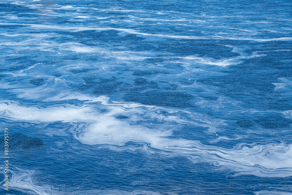 Tranquil and serene sunlit rippling water texture with abstract natural patterns and calm water details. Foam on the water from the fast river current. Tranquil and serene sunlit rippling water texture with abstract natural patterns and calm water details. Foam on the water from the fast river current.