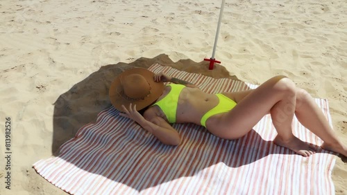 Hot young girl taking sunbath on beautiful coast summer weekend close up. slim lady wearing wide brimmed hat lying sand seashore enjoy sunlight. Sexy woman in swimsuit relax on beach top view.