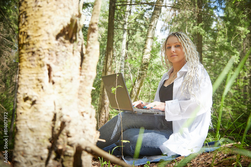 Girl with beautiful dreadlocks and laptop in green forest in spring or summer. Young IT woman, blogger working alone, blogging, chatting. Need for solitude photo