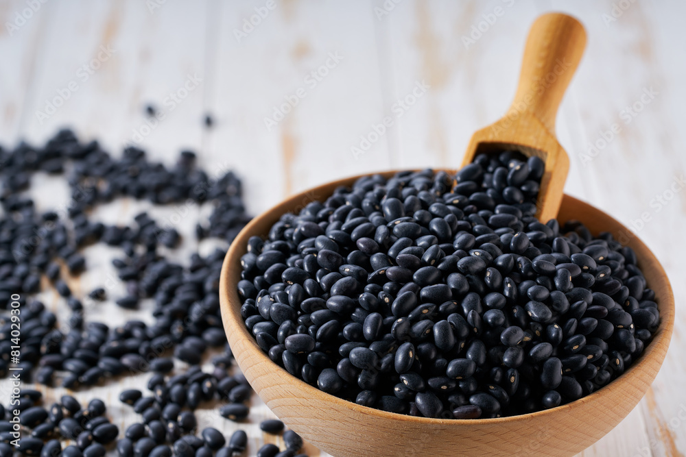 Raw black beans are scattered in a wooden bowl close up. Raw black beans are scattered in a wooden bowl close up.
