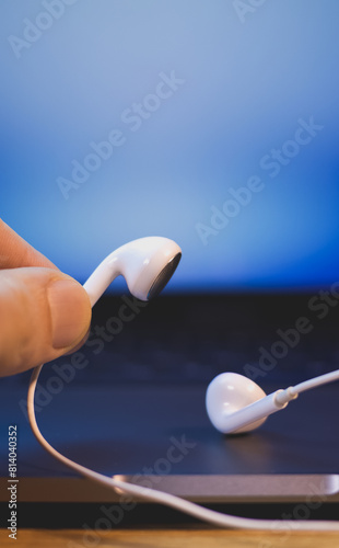 Man is holding White Earphones near the laptop. Modern music concept. Audio technology. Study and business concept.