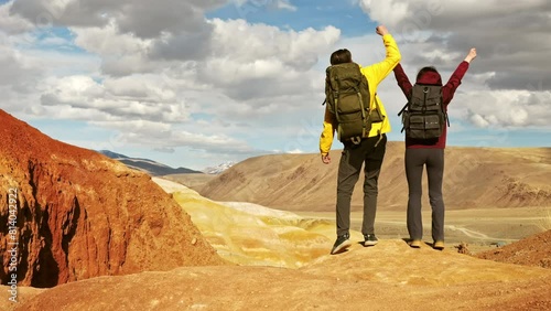 Back view at two young hikers celebrating peak achievement and raising arms, standing on high top of mountain. Motivation to travel success at scenic landscape
