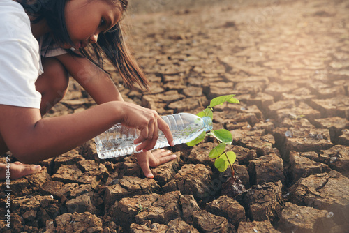 Asian girl planting tree and watering seedling on dry and crack ground to restore and change earth and environment. Drought and El Niño condition concept.