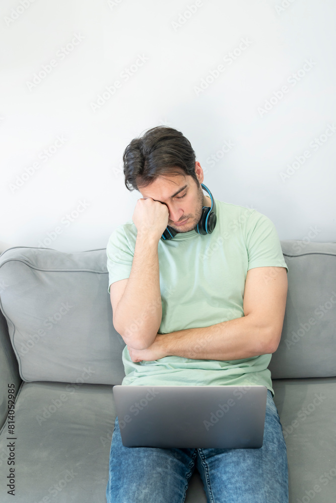 Fototapeta premium A young freelancer has a sore neck due to excessive work on his laptop at home. Concept of distance work and online learning