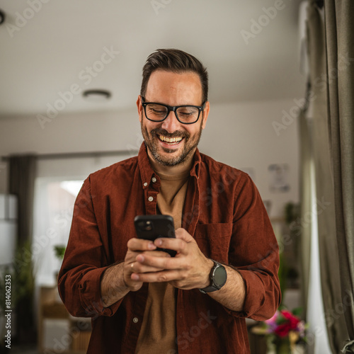Portrait of adult man stand and hold mobile phone text message at home
