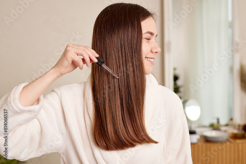 A young woman applies a drop of oil from a pipette to her hair, close-up. Vitamins, keratin for treatment, strengthening and growth of hair. Problems with dandruff, hair loss. Hair care concept
