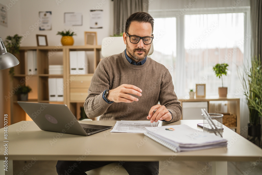 Adult businessman sit at office look on laptop hold paper at office Adult businessman sit at office look on laptop hold paper at office