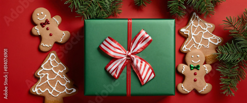 green gift box with a bow on a red background with Christmas tree flowers and ginger cookies. Decoration for Christmas