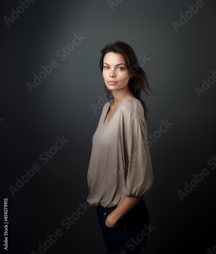 A brunette with wavy hair and a fleeting smile in light clothes on a gray background. Women's fashion and beauty, confident strong woman.