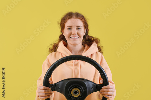 Pretty young woman with steering wheel on yellow background