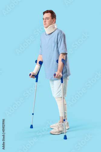 Injured young man after accident with crutches on blue background © Pixel-Shot