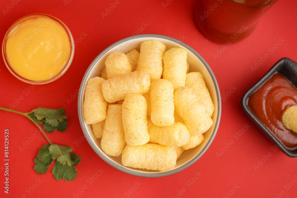Bowl with tasty salty corn sticks and sauces on red background, closeup Bowl with tasty salty corn sticks and sauces on red background, closeup