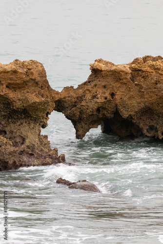 Views of the a Waves Crashing Along the Cliffside on an Overcast day in Albufiera Portugal photo