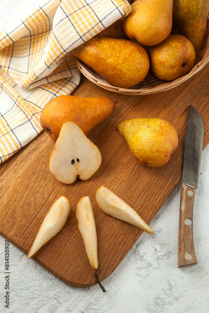 Cutting board with whole and slices pears, wicker basket and yellow kitchen towel on white wooden background.. Cutting board with whole and slices pears, wicker basket and yellow kitchen towel on white wooden background..