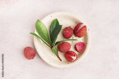 Plate with tasty litchi fruit and leaves on light background photo