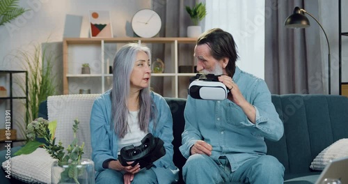 Mature couple man and woman talking before putting on special 3d glasses to watch virtual reality videos spending joint leisure at home