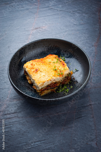 Traditional Greek moussaka with beef mince, eggplant and bechamel sauce served as close-up in a Nordic design Bowl on a stone board © HLPhoto