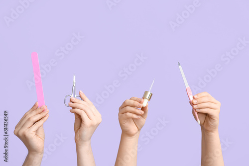 Female hands holding pipette with cuticle oil, scissors and nail files on lilac background photo