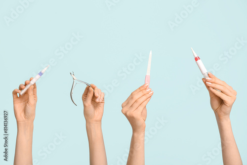 Female hands with cuticle oil pens, nail cutter and file on blue background