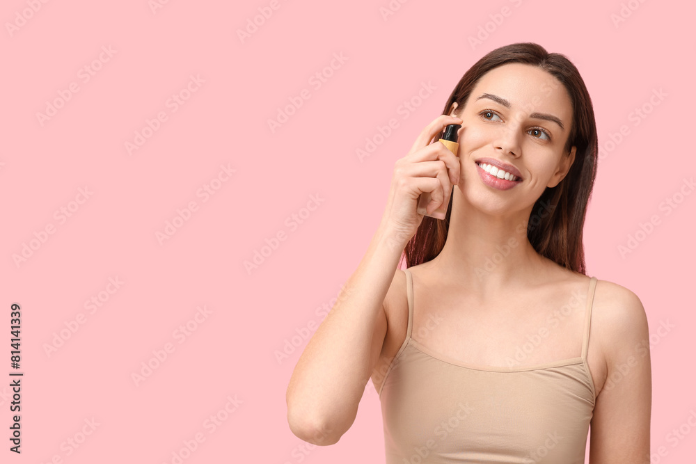 Beautiful young woman applying foundation on pink background Beautiful young woman applying foundation on pink background