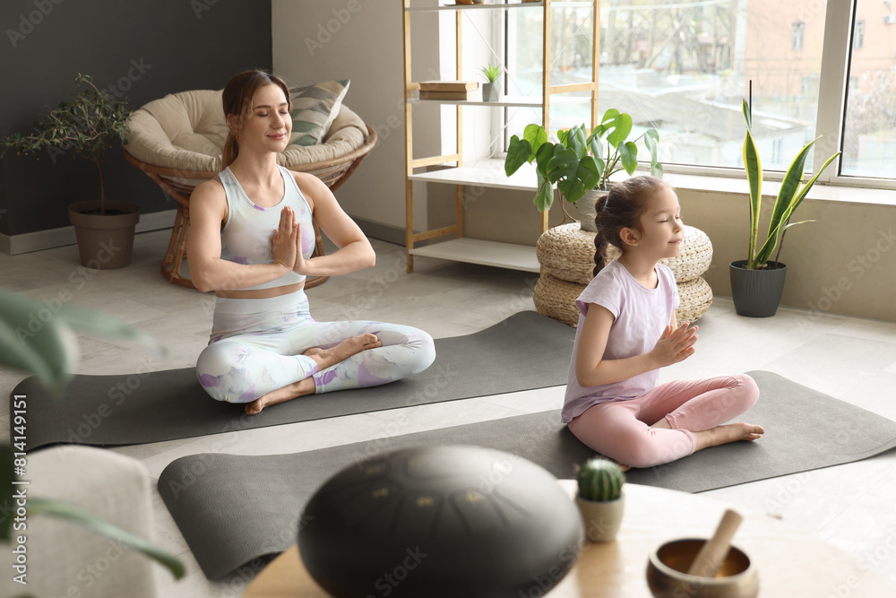 Sporty young woman with her little daughter meditating on yoga mats at home Sporty young woman with her little daughter meditating on yoga mats at home