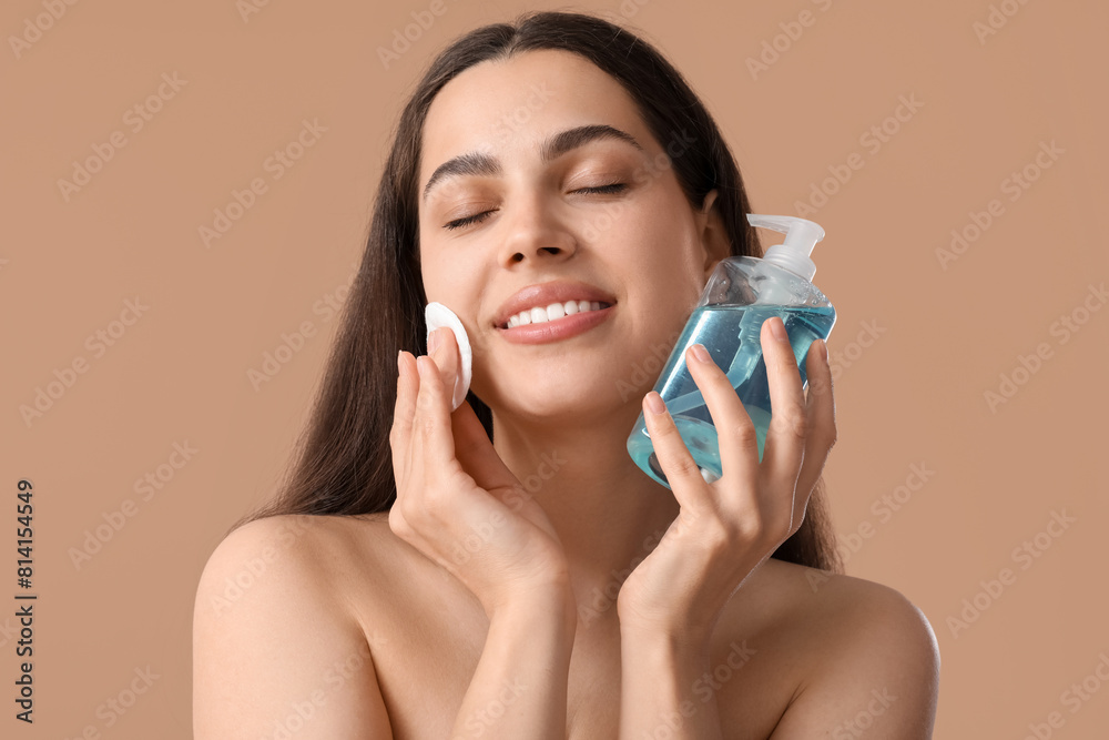 Beautiful young happy woman with cotton pad and bottle of micellar water on brown background Beautiful young happy woman with cotton pad and bottle of micellar water on brown background