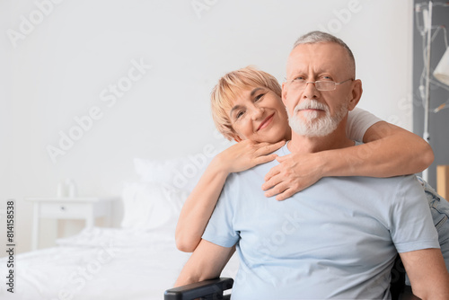 Mature woman hugging her sick husband in wheelchair at home