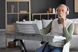 Mature man in headphones with microphone and synthesizer singing at home