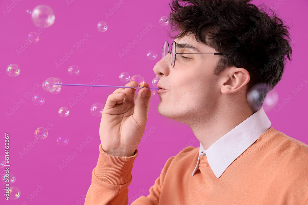 Male student blowing soap bubbles on purple background, closeup Male student blowing soap bubbles on purple background, closeup