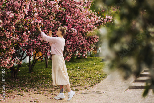 Young woman takes pictures on a smartphone of the beauty of spring pink blossoms.