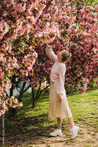 Vertical portrait of a young woman walking in the city among the spring pink blossoms of apple trees