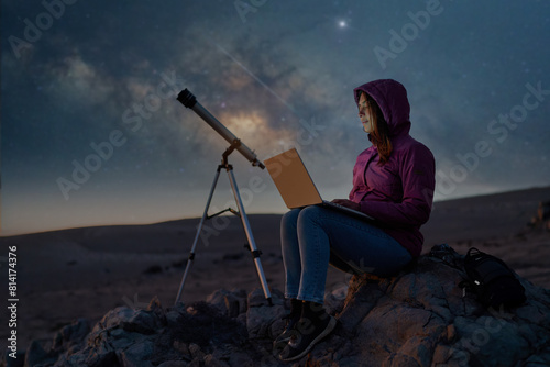 woman sitting in the desert with a laptop next to a telescope at night under the stars and milky way, astronomy and stargazing concept  photo