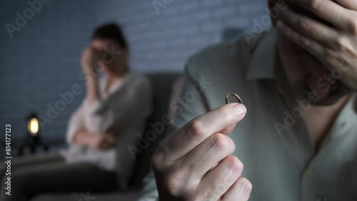 Upset husband during lovers conflict. A depressed man with a wedding ring with an offended woman in the background. photo