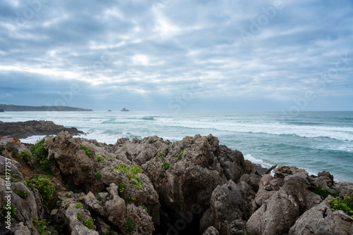 A rocky shoreline with brave waters on a day with a dramatic cloudy sky, Natural Park of the Dunes of Liencres, Cantabria, Spain